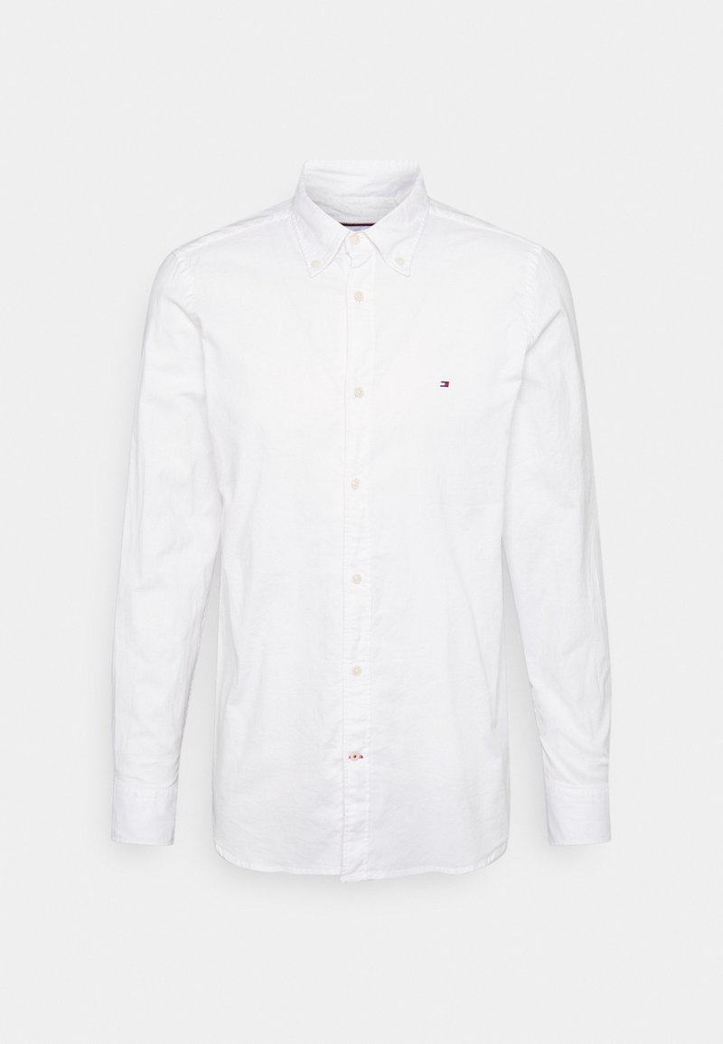 Chemise blanche à manches longues avec boutons, col et petit logo rouge, blanc et bleu sur le côté gauche de la poitrine.