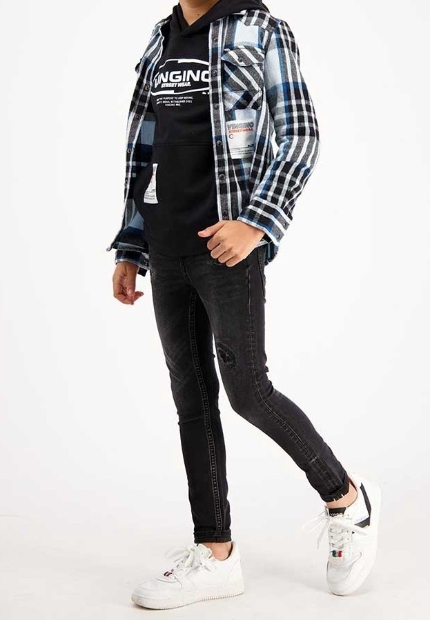 Chemise en flanelle à carreaux bleu et noir portée sur un sweat à capuche noir, associée à un jean noir slim et des baskets blanches avec des accents.