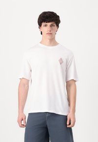 Camiseta de algodón blanca con cuello redondo y mangas cortas. Presenta un pequeño diseño bordado en rosa en el lado izquierdo del pecho.