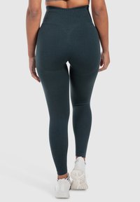 Hoge taille leggings in donkergroen, met een gladde textuur en naadloos ontwerp, gecombineerd met witte sportschoenen.