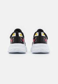Zapatillas negras con suelas blancas, con acentos gráficos coloridos y emojis en el talón, fabricadas con un tejido texturizado y un diseño deportivo.