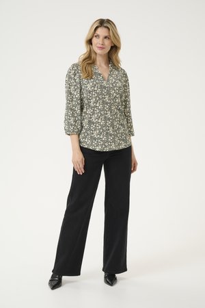 Blouse à imprimé floral avec des manches 3/4 en noir et blanc, design à col en V, accompagnée d'un pantalon large noir taille haute et de chaussures noires à talons pointus.