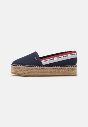 Marineblaue Espadrille mit gewebter Jute-Plateausohle, weißes und rotes Elastikband mit der Aufschrift "Tommy Jeans" an der Ferse.