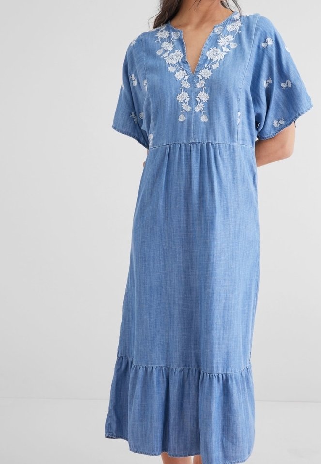Jeanskleid mit kurzen Ärmeln, V-Ausschnitt und weißer Blumenstickerei. Ausgestellter Saum mit Rüsche am unteren Ende. Weicher, leichter Stoff.