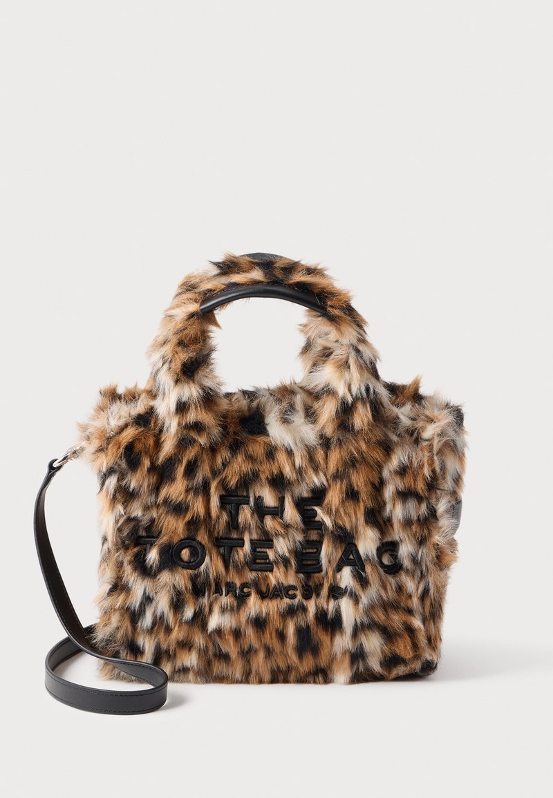 Petit sac fourre-tout recouvert de fausse fourrure tachetée marron et noire avec des anses en cuir noir et une bandoulière, avec un texte brodé noir.