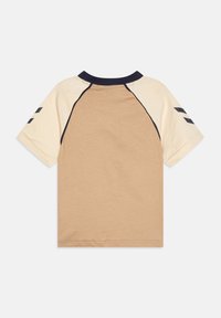 Beżowo-kremowa koszulka dziecięca z krótkim rękawem, z ciemnoniebieskim kołnierzykiem i czarnymi, szewronowymi paskami na rękawach, widoczna od tyłu.