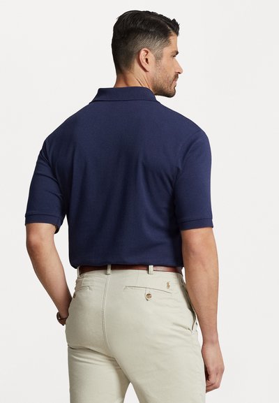 Polo de culoare bleu marin, cu mâneci scurte, guler plat și textură netedă. Asortat cu pantaloni bej deschis, care au două buzunare la spate și un logo.