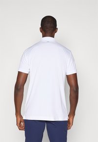 Hvit kortermet polo skjorte med krage, med en liten blå logo på baksiden, laget av et glatt, lett stoff.