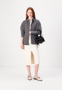 Sivi traper jakna, bijela bluzica, kremasto-midi suknja s prednjim prorezom i bež slingback cipele. Crna torba s uzorkom i nabranim detaljima.