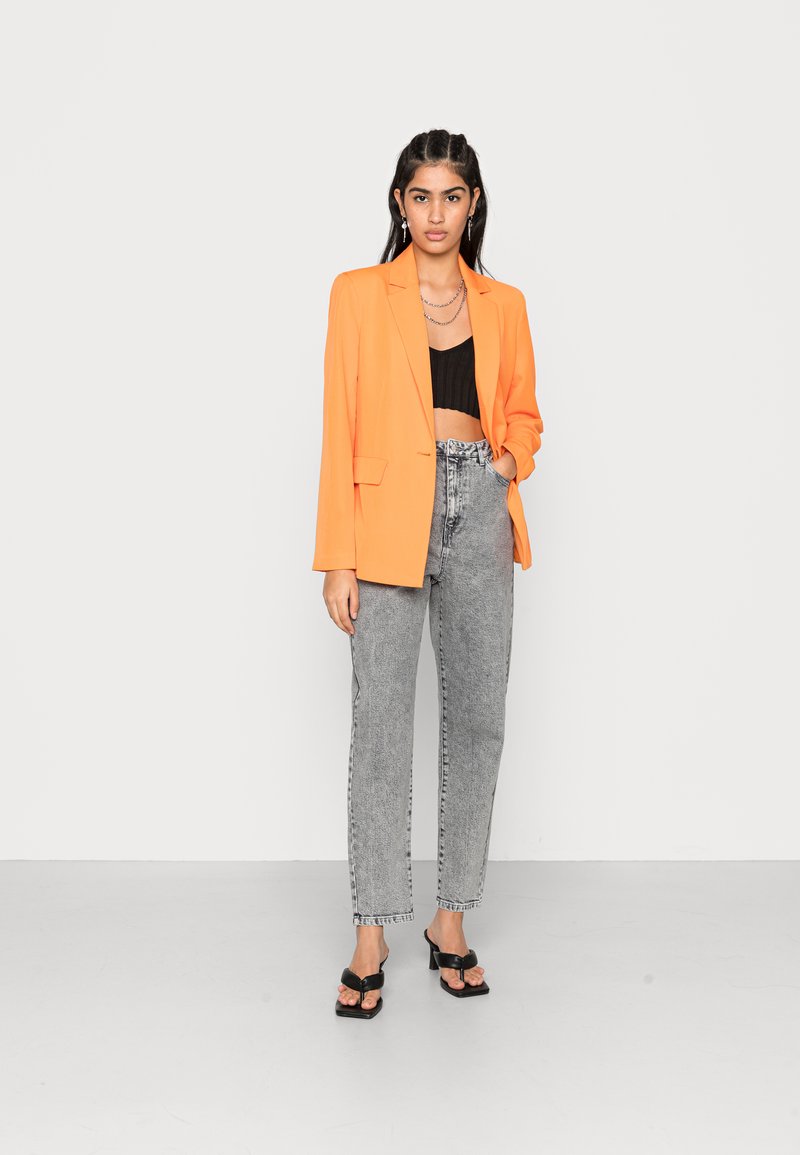Oranger oversized Blazer, schwarzes Cropped Top, hoch taillierte graue Jeans und schwarze Blockabsatzsandalen. Glatter Stoff, maßgeschneiderter Schnitt.