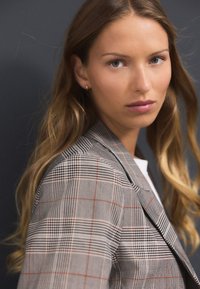 Checkered blazer in muted tones of gray, white, and red. Features a tailored fit with sharp lapels and structured shoulders.