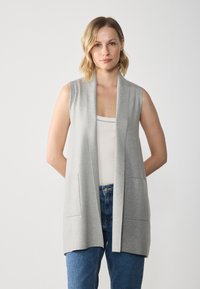 Light gray sleeveless cardigan with a deep V-neck, open front, and front pockets, made of soft knit fabric. Model wearing blue jeans.