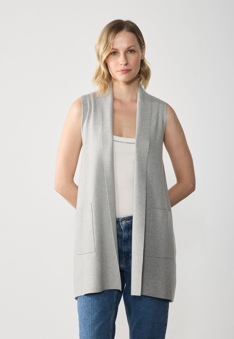 Light gray sleeveless cardigan with a deep V-neck, open front, and front pockets, made of soft knit fabric. Model wearing blue jeans.