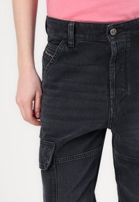 Pantalones cargo gris oscuro confeccionados en denim, con un bolsillo lateral, pasadores para cinturón y cierre de botón. Textura suave con detalles de costura sutil.