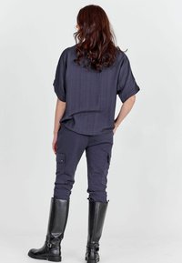 Tmavosivá, krátky rukáv, textúrovaná košeľa v kombinácii s tmavými cargo nohavicami a čiernymi čižmami po kolená. Neformálne oblečenie s funkčnými detailmi.