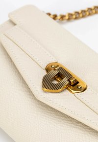Krémová kožená kabelka s texturou a zlatým zapínáním, zdobená geometrickým vzorem a řetízkem. Čisté linie a minimalisticé akcenty.