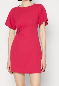Krótka różowa sukienka z krótkimi falbaniastymi rękawami, z detalem w postaci węzła w talii. Wykonana z gładkiego, elastycznego materiału.