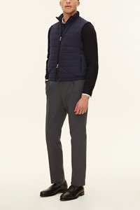 Marinblå vadderad väst med dragkedja framtill, lätt och quiltad design, bärs över en svart långärmad tröja, kombinerad med grå byxor och svarta skor.