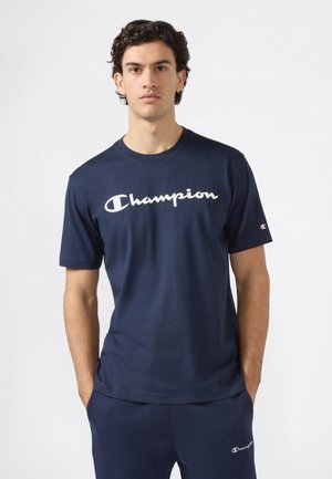 Camiseta de algodón azul marino con un destacado logo blanco de "Champion" en el pecho. Cuello redondo clásico y mangas cortas.