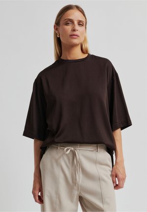 Kortermet, ledig svart bomulls-T-skjorte med rund hals. Brukt sammen med lyse beige bukser med snøring i livet.