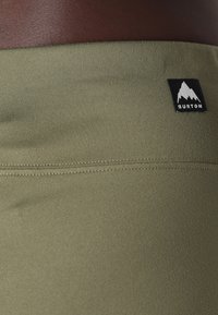 Olivengrønne atletiske shorts med en glat overflade, prydet med et sort Burton-logo og en kontrasterende brun talje.