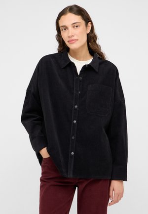 Black corduroy shirt with a collared neckline, front pocket, and button closure. Features a relaxed fit and ribbed texture.