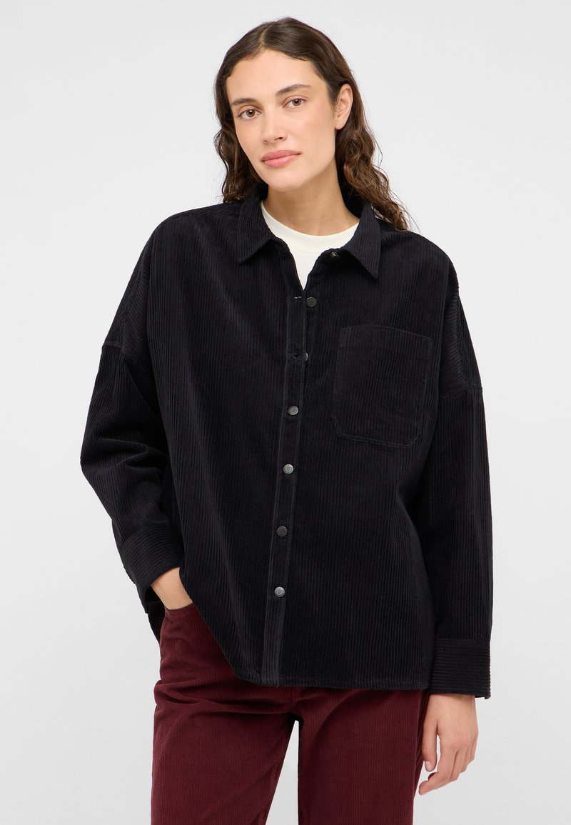 Cămașă din corduroy negru cu guler, buzunar frontal și închidere cu nasturi. Are o croială lejeră și o textură ribbată.