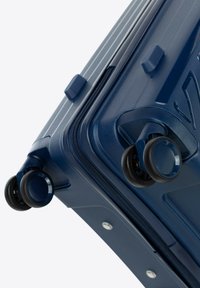 Navy blue hard-shell suitcase with textured stripes, dual wheels, and reinforced corners. Zipper closure with accented hardware details.