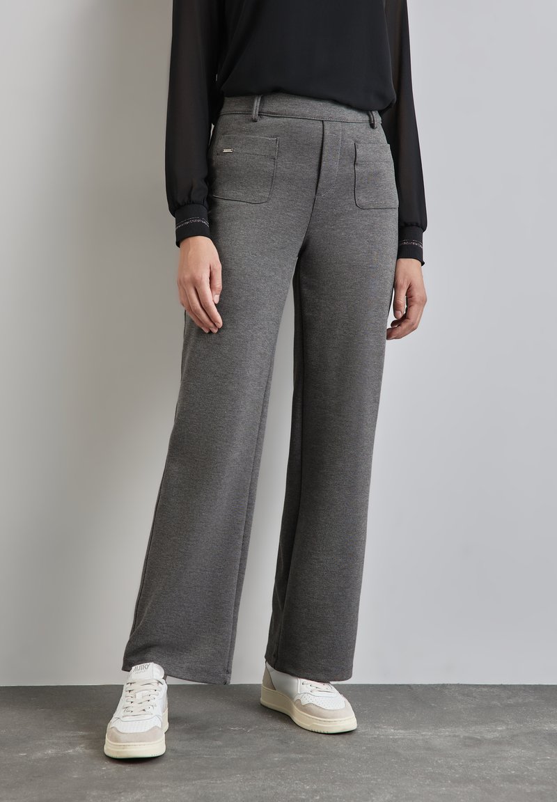Grijze wijde broek gemaakt van zachte stof, met twee zijzakken en een zachte tailleband, gecombineerd met witte sneakers.