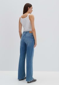 Jeans blu a vita alta con una vestibilità a gamba larga, caratterizzati da un classico design a cinque tasche e una toppa in pelle beige sulla cintura posteriore.