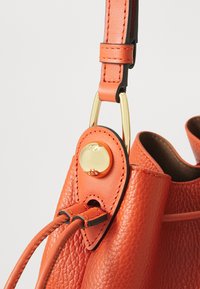 Borsa a mano in pelle arancione con una finitura texturizzata, accessori in oro e una tracolla con un design a cappio fissata da un bottone decorativo.