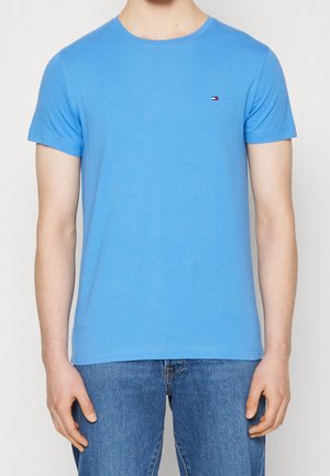 T-shirt en coton bleu clair avec un col rond, des manches courtes et un petit logo sur la poitrine. Texture douce. Coupe décontractée.