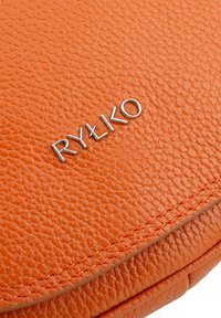 Orange leather bag with a textured surface, featuring silver metal branding "RYŁKO" prominently displayed. Notable stitching accent.