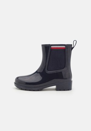 Botte cheville en caoutchouc bleu marine avec une finition brillante, des panneaux latéraux élastiques et une languette texturée au talon. Semelle légèrement surélevée et durable.