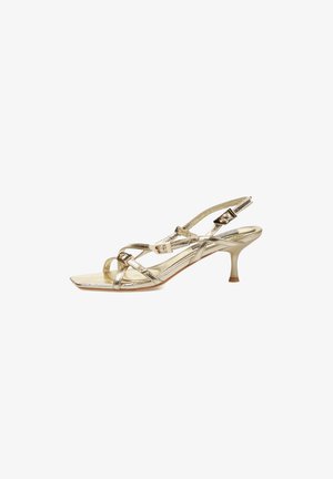 Sandalia dorada de tacón alto con tiras, puntera cuadrada, tres hebillas ajustables y tacón fino tipo kitten sobre fondo blanco.