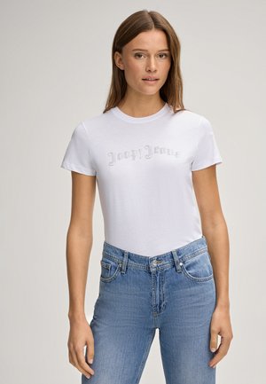 Witte t-shirt met korte mouwen gekenmerkt door een getextureerd scriptlogo in rhinestones, gecombineerd met hoge blauwe spijkerbroeken.