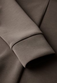 Tessuto di cotone marrone con un primo piano di un polsino, caratterizzato da una texture liscia e un sottile motivo a righe sulla manica.