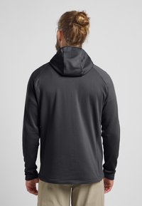 Veste à capuche noire avec un motif texturé, manches longues et un design ajusté, fabriquée en tissu léger et respirant.