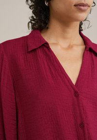 Bordo košulja na dugih rukava s teksturiranim materijalom, s kragnom i V izrezom, prikazana na neutralnoj pozadini.