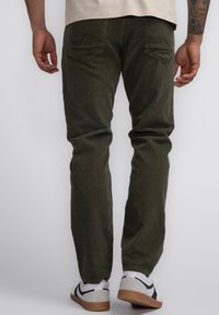 Olijfgroene corduroy broek met een ribbelstructuur, twee achterzakken en een slim fit. Draagt in combinatie met witte en zwarte sneakers.