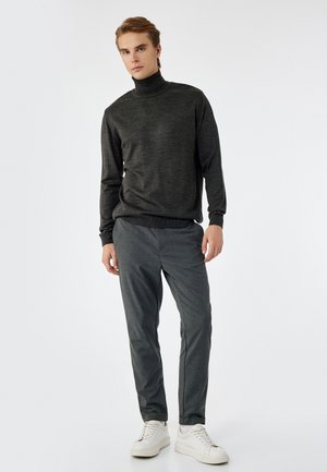 Suéter de cuello alto gris oscuro combinado con pantalones gris claro y zapatillas blancas. La tela parece suave, con puños y dobladillo acanalados.