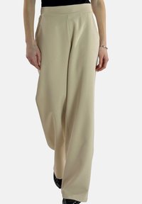 Beige wijde broek met een gladde textuur en een hoge tailleband. Voorzien van plooien en een ontspannen pasvorm, gecombineerd met zwarte schoenen.