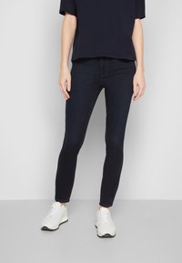 Jeans azul oscuro con corte ajustado, hechos de mezclilla, combinados con una camiseta navy y zapatillas blancas. Presentan una textura suave y costuras mínimas.