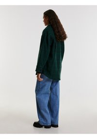 Groene en marineblauwe flanellen shirt met ruitpatroon, ruime pasvorm, met knoopsluiten aan de manchetten, gecombineerd met lichtblauwe denimjeans met wijde pijpen en zwarte platform schoenen.