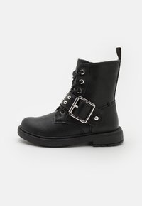 Botas de tobillo de cuero negro con un acabado texturizado, punta redonda, cordones en la parte delantera, detalle de hebilla plateada y suela de goma baja.