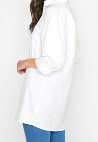 Lang�ärmliges weißes Button-Up-Hemd aus leichtem Baumwollstoff; bietet einen lockeren Schnitt, aufgerollte Ärmel und eine Brusttasche.