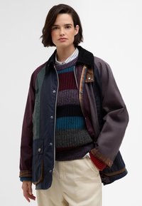 Színes foltvarrásos dzseki fekete kordbársony gallérral, nyomózáras zsebekkel és alatta többszínű csíkos kötött pulóverrel. Világos színű nadrág.