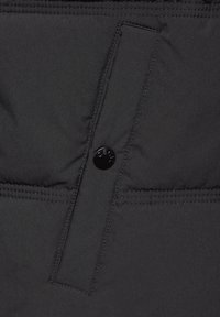 Schwarze gepolsterte Jacke mit glatter Textur, ausgestattet mit einem Knopfverschluss und sichtbaren Nähten, die ein elegantes und schlichtes Design hervorheben.