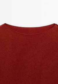 Gros plan sur un pull en tricot rouge avec un col rond, une texture douce et un motif régulier partout. Les bords sont soigneusement finis.