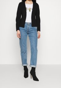 Black blazer, white T-shirt with cactus graphic, light blue cuffed jeans, and black pointed ankle boots. Smooth fabric, tailored fit.